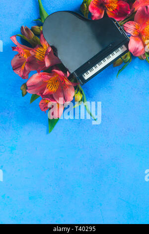 Piccolo pianoforte con molla alstroemeria fiori su uno sfondo blu con copia spazio. Primavera o estate festival musicale di concetto con spazio di copia Foto Stock