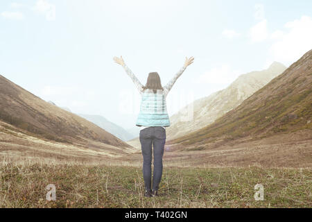 Una ragazza in montagna una vista dal retro con le braccia sollevate gioisce conseguimento Foto Stock