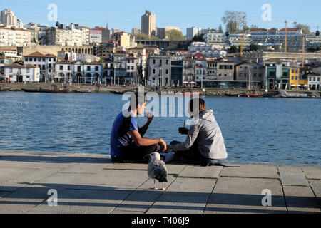 Una giovane coppia seduta che mangiano insieme sulla banchina dal fiume Douro su una molla pomeriggio nella città di Porto, Portogallo Europa KATHY DEWITT Foto Stock