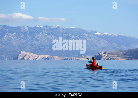 Donna kayak tra belle isole croate, montagna Velebit in background, Croazia, Krk. Foto Stock