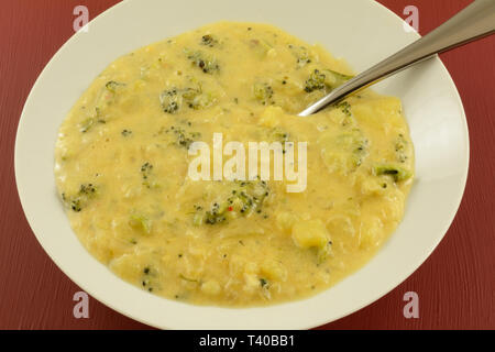 Di broccoli e patate Zuppa di formaggio zuppa in tazza bianca con cucchiaio in sfondo rosso Foto Stock