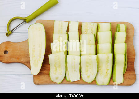 Zucchina tagliata con nastri utilizzando frese vegetali. Situato su una tavola di legno su uno sfondo bianco, vista dall'alto Foto Stock