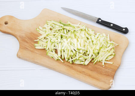 Zucchina tagliata a strisce sottili, disposti su una tavola di legno su sfondo bianco, vista dall'alto, e vi è inoltre un coltello accanto Foto Stock