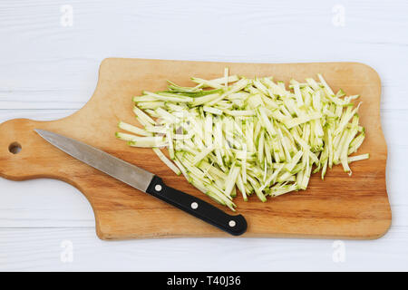 Zucchina tagliata a strisce sottili, disposti su una tavola di legno su sfondo bianco, vista dall'alto, e vi è inoltre un coltello accanto Foto Stock