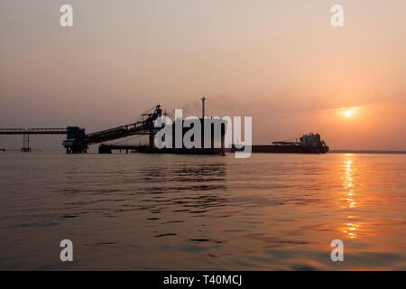 Operazioni portuali per la gestione e il trasporto di minerali di ferro all'alba e tramonto con 2 navi TSV - uno al molo di carico, uno in attesa di dock. Sierra Leone Foto Stock