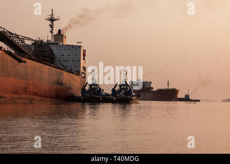 Operazioni portuali per la gestione e il trasporto di minerali di ferro all'alba e tramonto con 2 navi TSV - uno al molo di carico, uno in attesa di dock. Sierra Leone Foto Stock