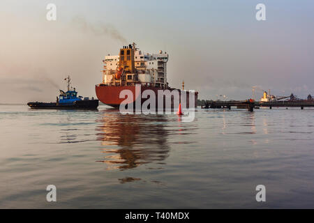 Operazioni portuali per la gestione e il trasporto di minerale di ferro. Rimorchiatore di spinta e movimentazione transhipper vaso da dock a layby jetty prima di passare al molo di carico Foto Stock