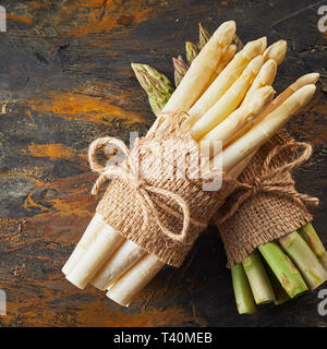 Chiudere su un bundle di prodotti freschi Asparagi bianchi spears poggiato su di un secondo verde uno sotto legato con una corda e hessian su un metallo arrugginito sfondo Foto Stock