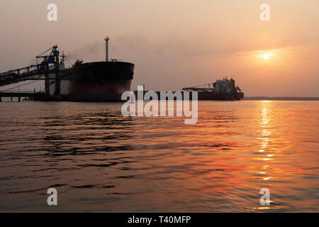 Operazioni portuali per la gestione e il trasporto di minerali di ferro all'alba e tramonto con 2 navi TSV - uno al molo di carico, uno in attesa di dock. Sierra Leone Foto Stock