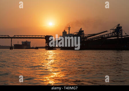 Operazioni portuali per la gestione e il trasporto di minerali di ferro all'alba e tramonto con 2 navi TSV - uno al molo di carico, uno in attesa di dock. Sierra Leone Foto Stock
