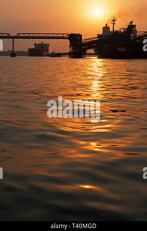 Operazioni portuali per la gestione e il trasporto di minerali di ferro all'alba e tramonto con 2 navi TSV - uno al molo di carico, uno in attesa di dock. Sierra Leone Foto Stock