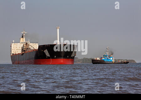 Operazioni portuali per la gestione e il trasporto di minerale di ferro. Il trasbordo in barca e tug prepararsi a salpare per scaricare in OGV - Ocean andando peschereccio in mare Foto Stock