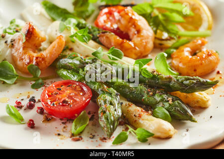 Gourmet di gamberi freschi e il verde e bianco antipasto di asparagi conditi con spezie e guarnita con erbe in un vicino la vista ritagliata su un ritardo Foto Stock