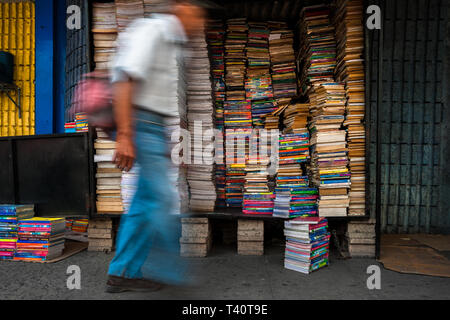 Un vescovo salvadoregno uomo cammina davanti a pile di libri usati impilati in una scatola per strada in una libreria di seconda mano in San Salvador El Salvador. Foto Stock