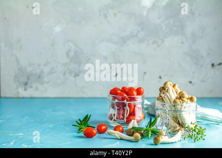 Buna Shimeji - funghi commestibili dall Asia orientale. Buon cibo per una buona salute. Intrico di funghi shimeji e pomodori ciliegia in vasi sul blu surfa in calcestruzzo Foto Stock