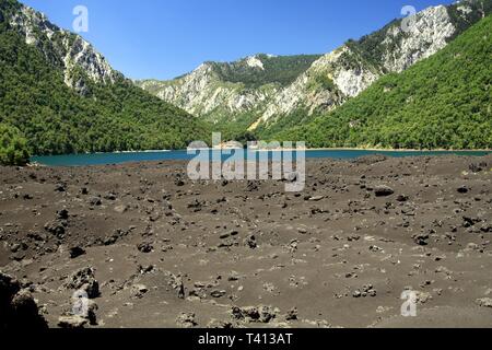 Vista sulle ceneri vulcaniche su isolato blu appartato il cratere del lago circondato da montagne nel centro del Cile a Conguillio NP Foto Stock