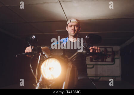 Uomo che fissa la bicicletta. Fiducioso giovane uomo che ripara moto presso il suo garage. Foto Stock