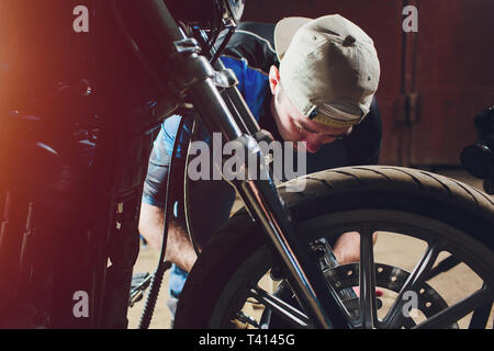 Uomo che fissa la bicicletta. Fiducioso giovane uomo che ripara moto presso il suo garage. Foto Stock