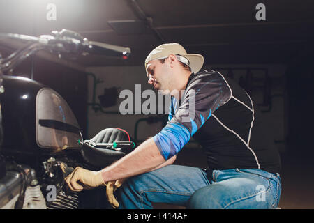 Uomo che fissa la bicicletta. Fiducioso giovane uomo che ripara moto presso il suo garage. Foto Stock