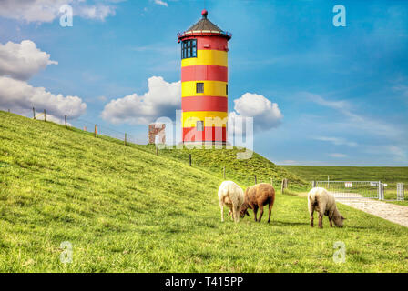 Le pecore di fronte al Pilsum faro sulla costa del Mare del Nord della Germania. Foto Stock