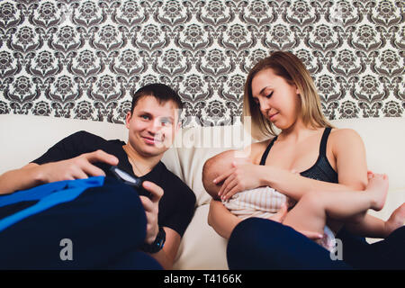 Famiglia siede sul lettino, un uomo gioca nella console. Foto Stock