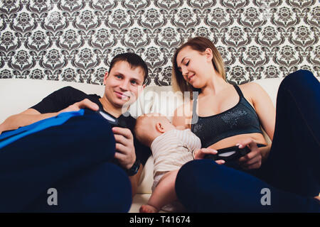 Famiglia siede sul lettino, un uomo gioca nella console. Foto Stock