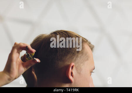 Ritratto di giovane uomo avente taglio di capelli in un barbiere. Parrucchiere uomo taglio di capelli con le forbici. Foto Stock