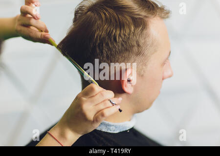 Ritratto di giovane uomo avente taglio di capelli in un barbiere. Parrucchiere uomo taglio di capelli con le forbici. Foto Stock