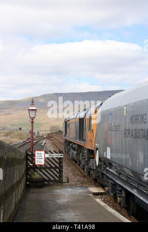 Classe 66 GBRf locomotiva diesel-elettriche trasporta un treno di pietra attraverso Ribblehead stazione da stabilirsi a Carlisle linea ferroviaria il 12 aprile 2019. Foto Stock