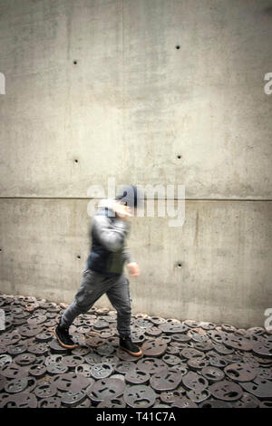 La figura sfocata camminare su crani di metallo, parte di un'installazione presso il Museo Ebraico di Berlino Foto Stock