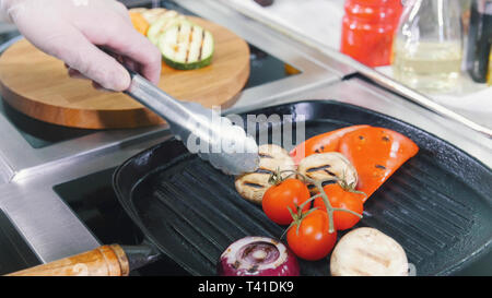 Un lavoro dello chef in cucina. Riscaldamento dei funghi e verdure in padella Foto Stock