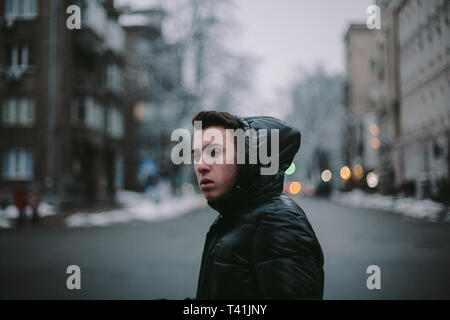 Vista laterale del giovane uomo attraversando una strada di città in inverno Foto Stock
