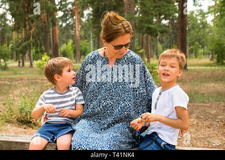 Due simpatici ragazzi a parlare con un infermiere, nonna. I bambini di ridere nel parco, giardino, foresta. Un genitore di famiglia. I fratelli l'amore. I fratelli colloqui. Felice Foto Stock