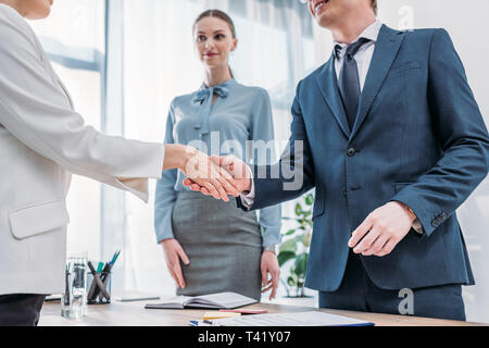 Vista ritagliata della allegro reclutatore stringono le mani con la donna vicino attraente collega in ufficio Foto Stock