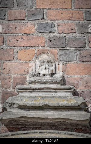 Stonr scultura di un teschio umano insieme contro un mattone rosso sfondo a parete. Foto Stock