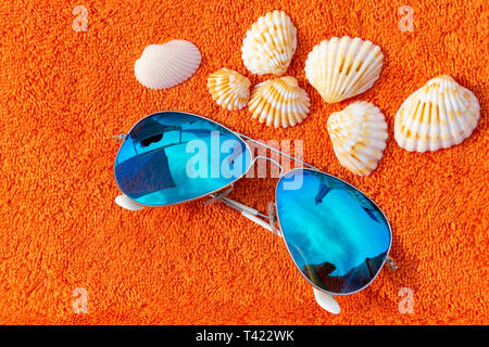 Moda sunglases vicino a conchiglie sulla spiaggia arancione asciugamano. Fotografia concettuale suggerendo le vacanze estive e il tempo per il relax e la pastella di carica Foto Stock