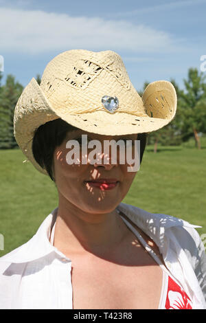 Dai capelli scuri bella donna in posa di un parco che indossa un cappello di paglia Foto Stock