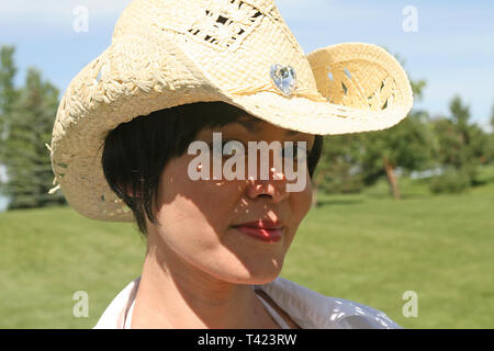 Dai capelli scuri bella donna in posa di un parco che indossa un cappello di paglia Foto Stock