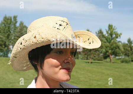 Dai capelli scuri bella donna in posa di un parco che indossa un cappello di paglia Foto Stock