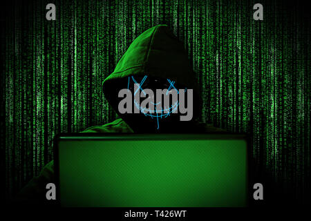 Hacker con incandescente maschera dietro notebook portatile di fronte fonte verde codice binario internet sfondo cyber attacco hack il concetto di computer Foto Stock