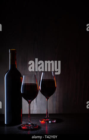 Due bicchieri e una bottiglia di vino rosso su uno sfondo di legno Foto Stock