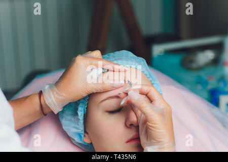 Medico dando face lifting di iniezione sul metà donna età nella fronte tra le sopracciglia per rimuovere le rughe di espressione in una clinica di chirurgia O.R camera Foto Stock