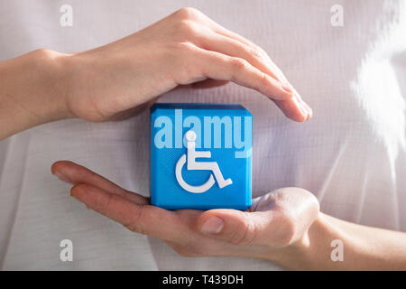 Close-up di un essere umano la mano la protezione blu blocco cubico con disabili Icona Handicap Foto Stock