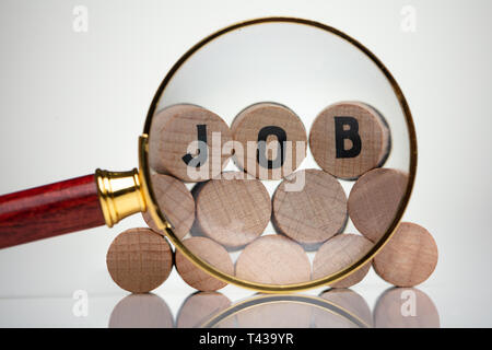 Close-up di un testo di lavoro dei blocchi di legno dietro la lente di ingrandimento su sfondo bianco Foto Stock