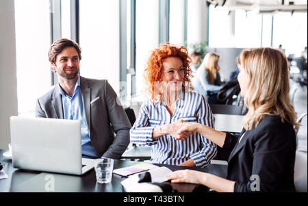 Un gruppo di giovani uomini di affari che seduto in un ufficio, scuotendo le mani. Foto Stock