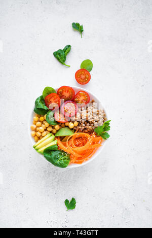 Ciotola di Buddha con insalata di grano saraceno, avocado, carote, pomodoro, spinaci, ceci su grigio. Vegetariano sana dieta vegana mangiare, super cibo. Vista superiore, copia Foto Stock