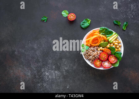 Ciotola di Buddha con insalata di grano saraceno, avocado, carote, pomodoro, spinaci, ceci su nero. Vegetariano sana dieta vegana mangiare, super cibo. Vista superiore, cop Foto Stock