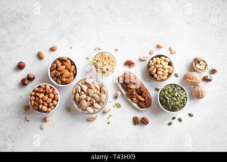 Vari dadi in bocce su sfondo bianco, vista dall'alto, copia dello spazio. Dadi assortimento - le noci pecan, nocciole, noci, pistacchi, mandorle, pinoli, arachidi Foto Stock