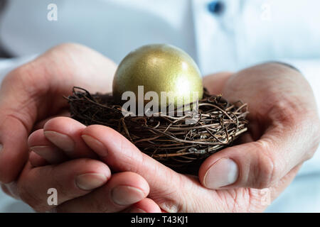 Close-up di umana con le mani in mano azienda Golden Egg nel nido di piccole dimensioni Foto Stock