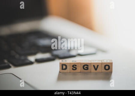 Cubi di legno con le lettere "DGSVO" per Datenschutzgrundverordnung sono giacenti su un computer portatile Foto Stock